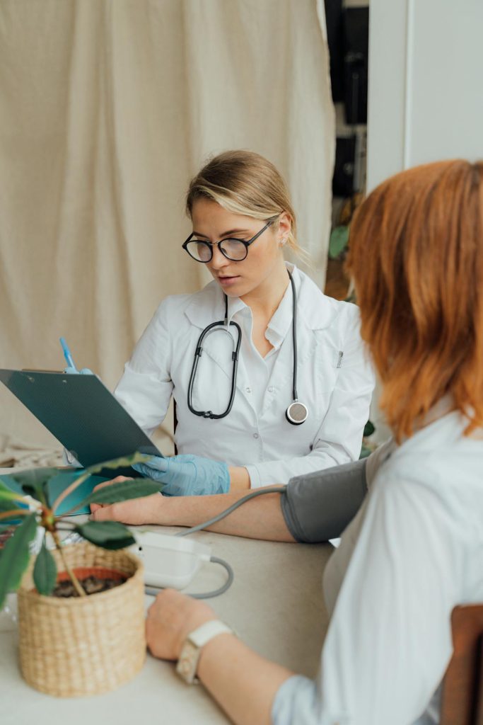 A doctor in a white coat checking a patient's blood pressure while discussing symptoms in a clinic.